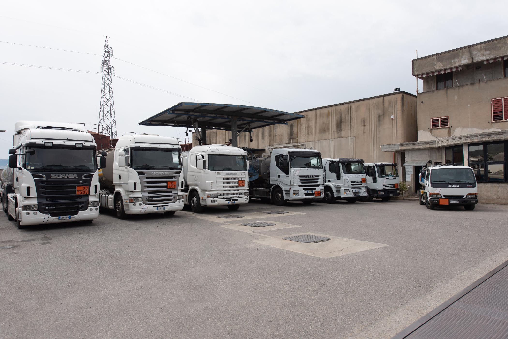 Autocisterne Scania, Iveco e Isuzu bianche con pannelli arancioni sotto la pensilina del deposito FA Petroli